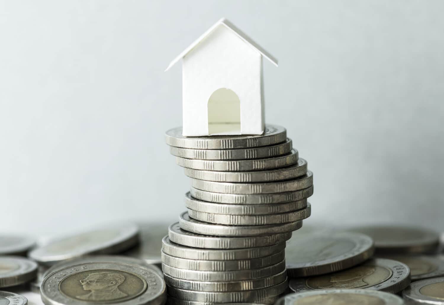 Miniaturhaus auf einem Stapel Münzen – symbolisiert Hausfinanzierung und Kapitalbedarf beim Hausbau